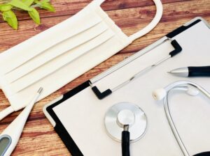 木目のテーブルに置かれた聴診器とマスク、体温計