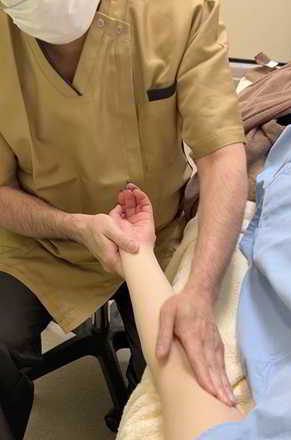 イランカラプテマッサージの施術風景。患者の左腕をやさしく軽擦し、自律神経を整える皮膚刺激を行っている様子（ぴりか治療院）